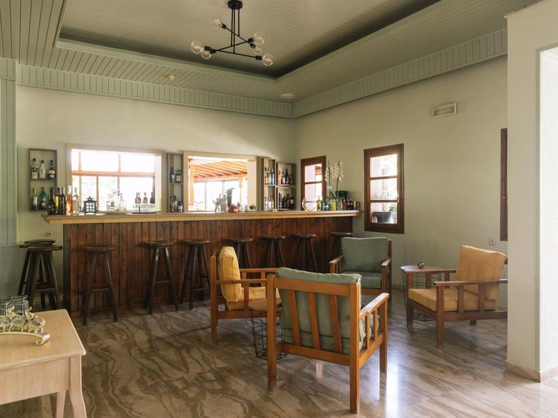 Lichte hotellounge met houten bar, fauteuils en groot raam met uitzicht op het buitengebied.