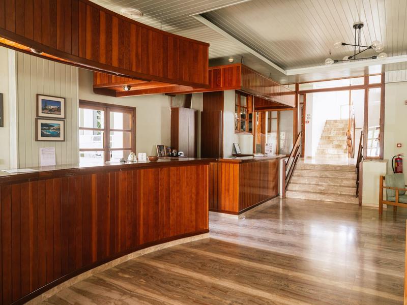 Lichte hotelreceptie met houten balie, trap en stoelen.