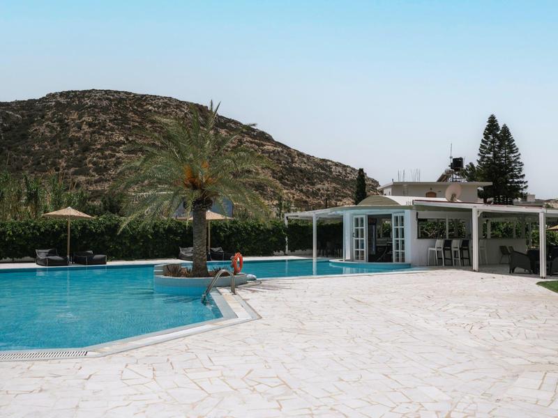 Zwembad met parasols voor een hut en heuvels op de achtergrond.