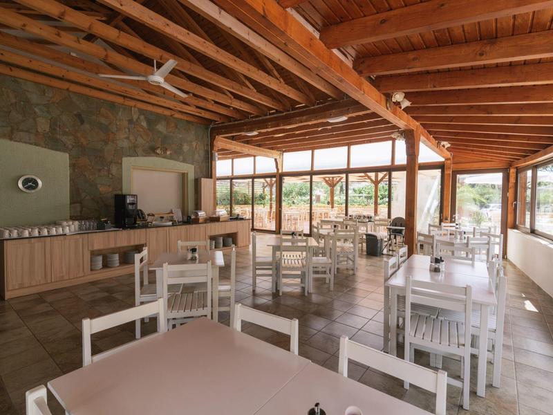 Licht restaurant met houten balkenplafond en grote ramen met uitzicht op groen.