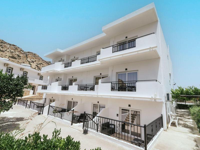 Modern wit hotelgebouw met drie verdiepingen en balkons onder een heldere blauwe lucht.