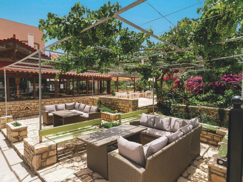 Buitenzitgedeelte met banken, paviljoenen en veel groen in een zonnige hoteltuin.