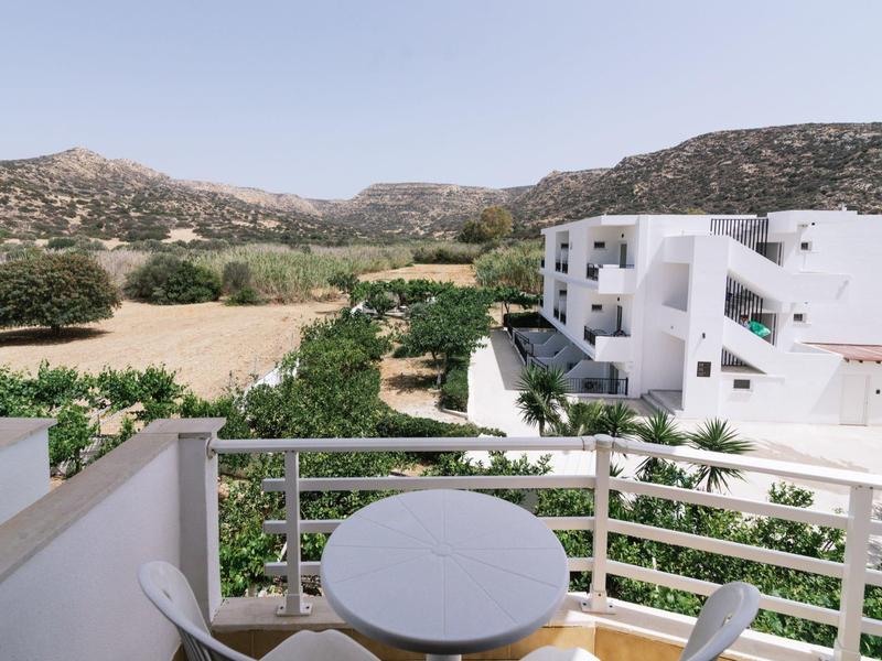 Balkon met tafel en twee stoelen met uitzicht op groen landschap en witte gebouwen.