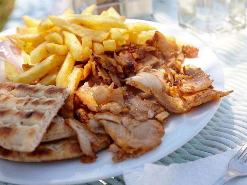 Bord met frietjes, platbrood en gegrild vlees op een buitentafel.