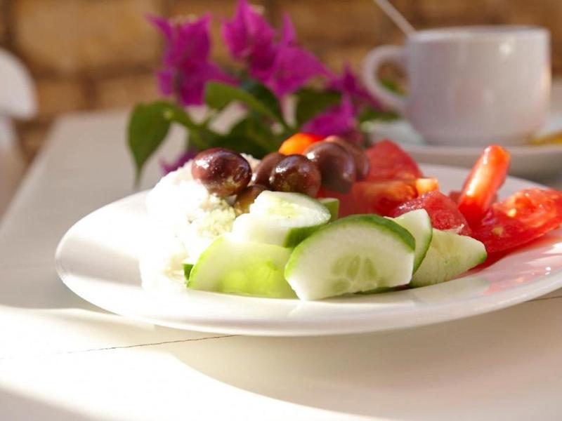 Een bord met verse groenten, olijven en tzatziki op een tafel in zonlicht.