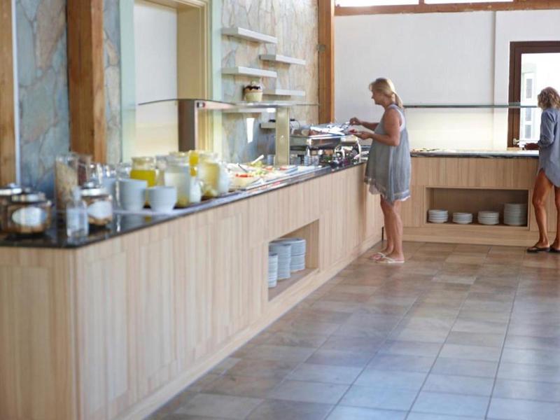 Twee vrouwen bedienen zichzelf bij een buffet in een lichte ontbijtzaal met houten lambrisering.