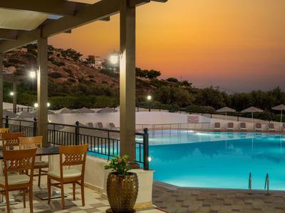 Terrazza serale con tavoli in legno vista piscina illuminata e colline.