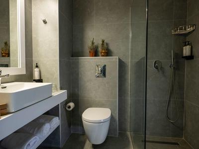 Bagno moderno in hotel con piastrelle grigie, doccia a filo pavimento e wc bianco.