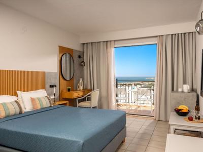 Lichte hotelkamer met tweepersoonsbed, bureau en balkon met uitzicht op zee.