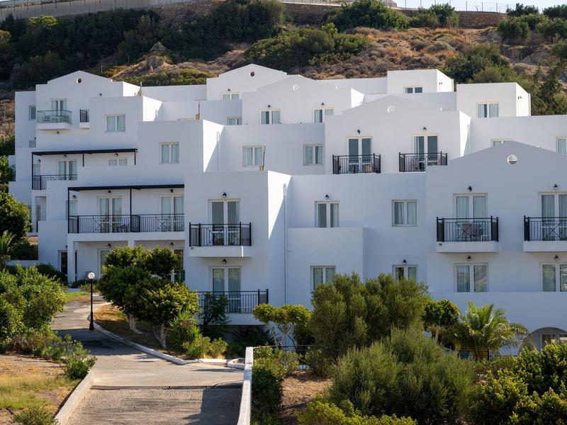 Edifici bianchi di un hotel con balconi in un paesaggio collinare verde illuminato dal sole.