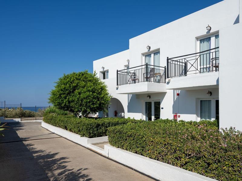 Edificio bianco con balconi sotto un cielo azzurro limpido e cespugli verdi ben curati.