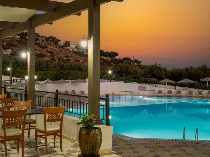 Terrazza serale con tavoli in legno vista piscina illuminata e colline.