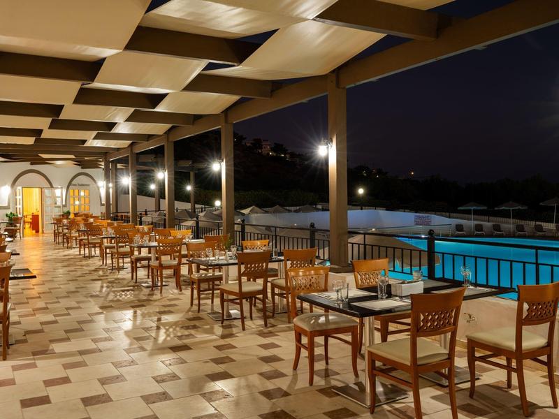 Terrazza coperta con tavoli apparecchiati accanto a una piscina illuminata di notte.