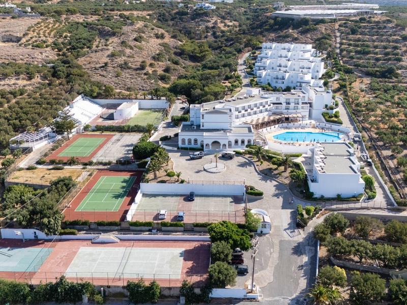 Veduta aerea di un hotel con campi da tennis, piscina e paesaggio mediterraneo circostante.