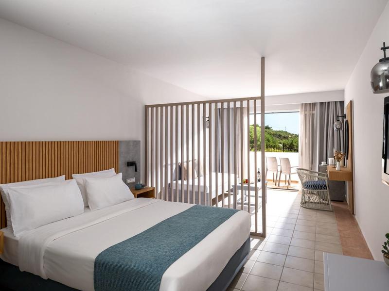 Camera d'hotel moderna con letto matrimoniale, accenti in legno e balcone con vista sul verde.