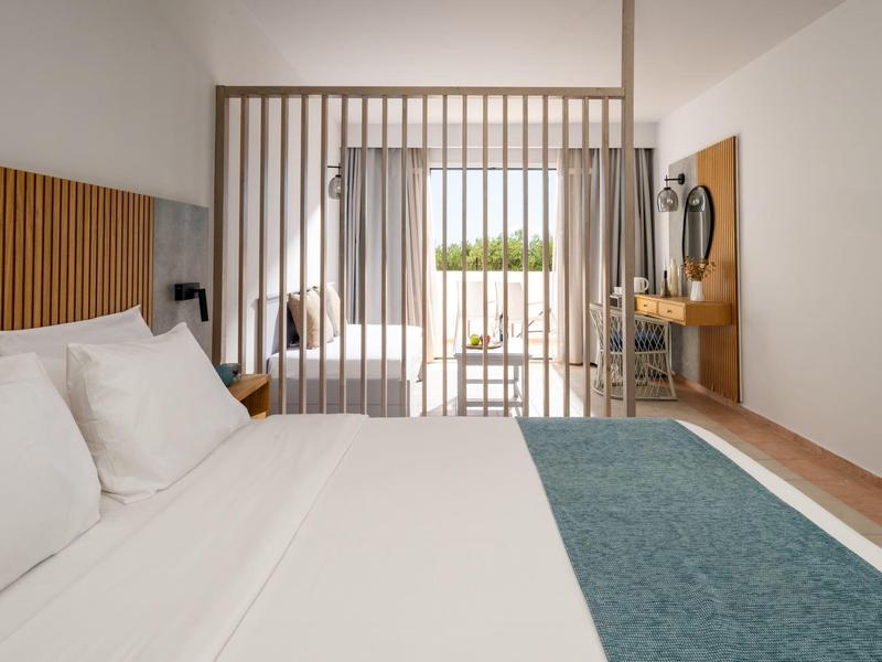 Camera d'hotel moderna con letto bianco, copriletto verde e vista sul balcone attraverso la parete divisoria