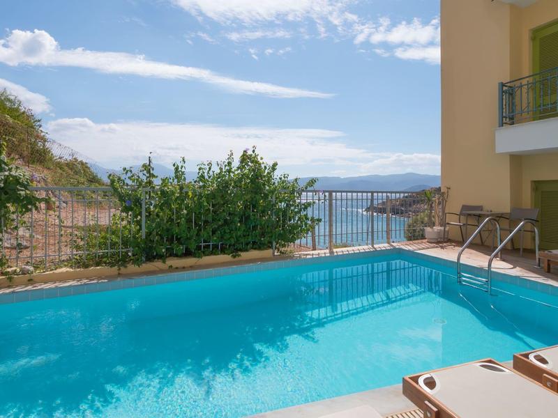 Klares Schwimmbad mit Liegestühlen neben einem Hotelgebäude mit Blick auf das Meer.
