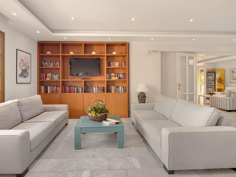 Heller Wohnbereich mit zwei grauen Sofas, grünem Couchtisch und eingebautem Holzbücherregal mit Fernseher.