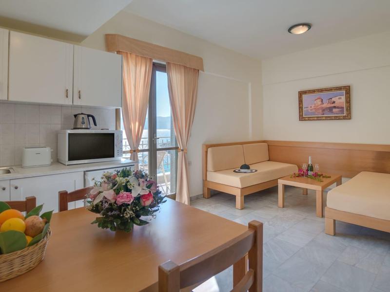 Helles Hotelzimmer mit einem Tisch, Stühlen, Sofaecke und Balkon mit Gardinen.