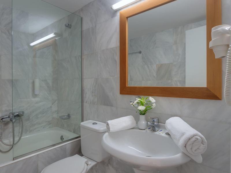 Modernes Hotelbadezimmer mit Badewanne, Toilette und Waschbecken mit Handtüchern und Blumen.