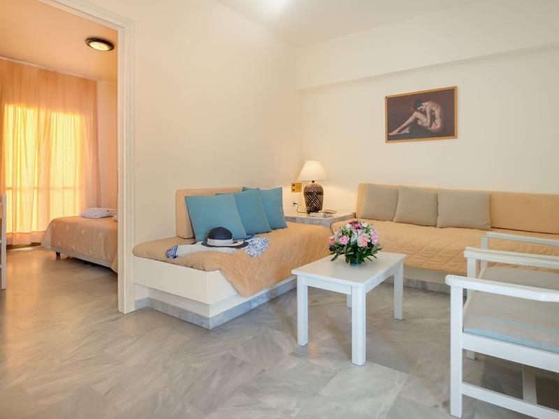 Helles Wohnzimmer mit Ecksofa, Sesseln und Tisch, Blick ins Schlafzimmer mit Vorhängen.