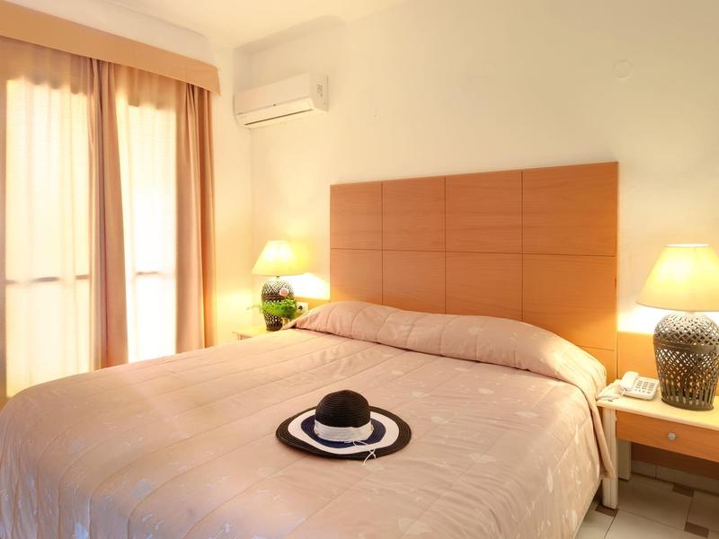 Helles Hotelzimmer mit Doppelbett, Holz-Kopfteil und zwei Nachttischen mit Lampen.