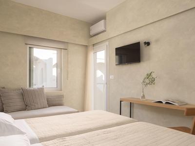 Nowoczesny, jasny pokój hotelowy z dwoma łóżkami, siedziskiem przy oknie i telewizorem na ścianie.