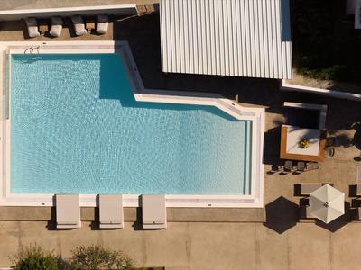 Widok z drona na prostokątny basen z leżakami i parasolami obok strefy hotelowej.