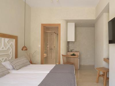 Nowoczesny pokój hotelowy z łóżkiem podwójnym, telewizorem, biurkiem i łazienką z szklanymi drzwiami.