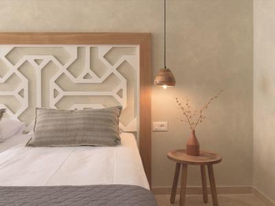 Przytulna sypialnia z białym łóżkiem, szarymi poduszkami i małym drewnianym stolikiem z wazonem.