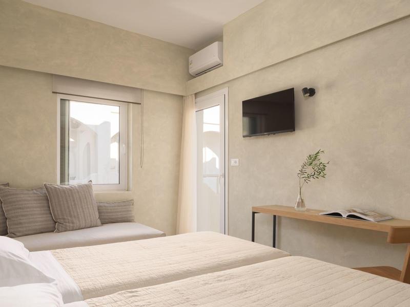 Nowoczesny, jasny pokój hotelowy z dwoma łóżkami, siedziskiem przy oknie i telewizorem na ścianie.