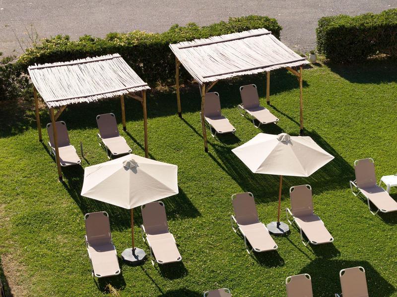 Leżaki z białymi parasolami i drewnianymi daszkami na zielonym trawniku.