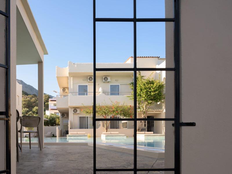 Widok przez bramę na basen przed wielopiętrowym budynkiem hotelu w słoneczny dzień.