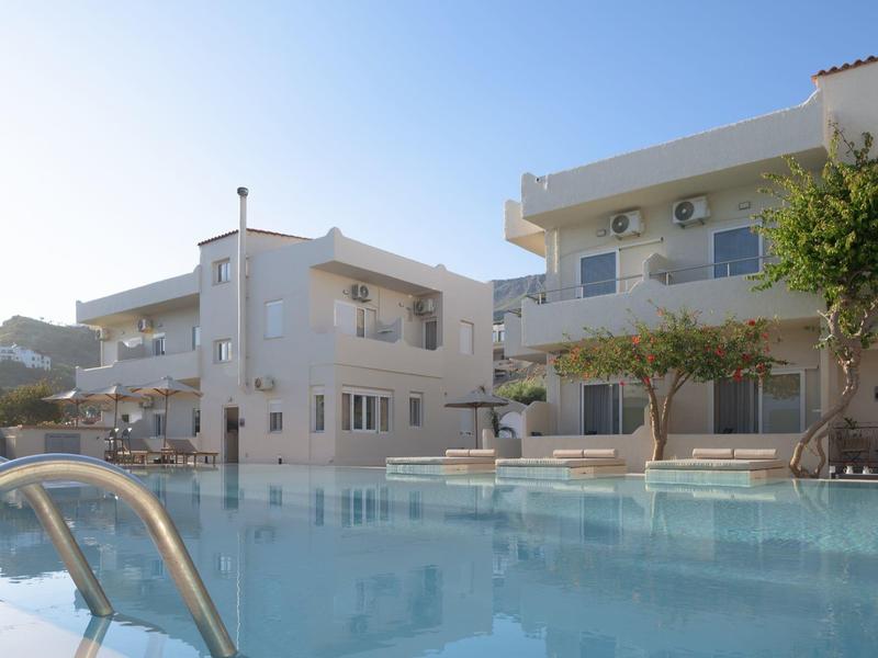 Nowoczesny kompleks hotelowy z basenem pod niebieskim niebem i leżakami przy wodzie.