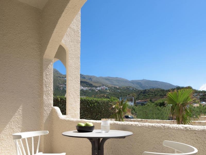 Balkon z białymi krzesłami i małym stolikiem z widokiem na góry przy czystym niebie.