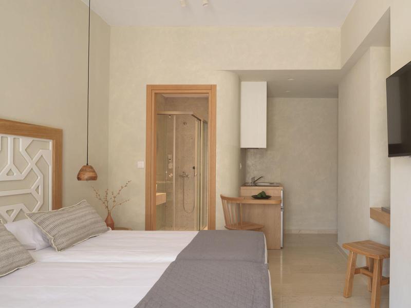 Nowoczesny pokój hotelowy z łóżkiem podwójnym, telewizorem, biurkiem i łazienką z szklanymi drzwiami.