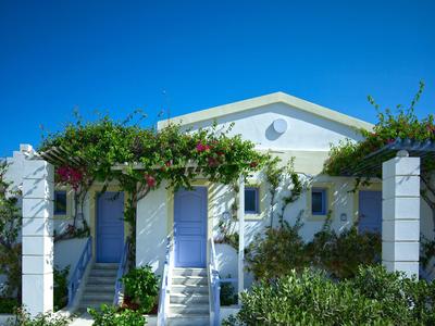 White building with blue doors and lush green vegetation under clear blue sky.