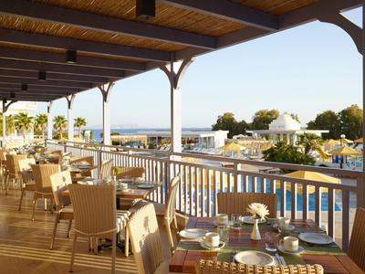 Hotel balcony with set tables overlooking pool and sea.