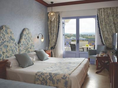 Brightly furnished hotel room with double bed, balcony, and view of the landscape.