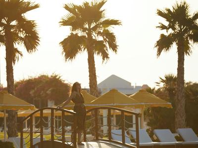Coucher de soleil sur une zone de piscine d'hôtel avec des palmiers et des parasols jaunes.