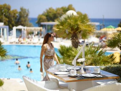 Table with tea set by the pool, woman nearby, sea visible in the background.
