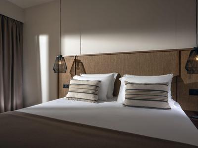 Chambre d'hôtel confortable avec grand lit, oreillers décoratifs et lampes suspendues modernes.