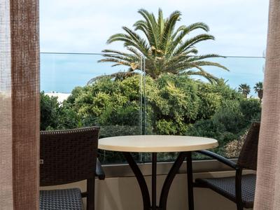 Table de balcon avec deux chaises devant un décor de palmiers et ciel bleu.