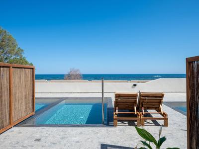 Zwei Liegestühle neben einem kleinen Pool mit Blick auf den Strand und das Meer.