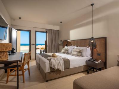 Modern eingerichtetes Hotelzimmer mit großem Bett, Schreibtisch, Fernseher und Blick auf den Strand.