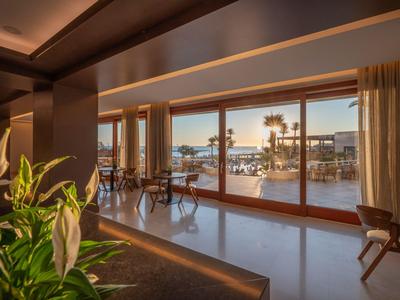 Moderner Hotelbereich mit Pflanzen, Glasfront und Blick auf einen sonnigen Poolbereich mit Palmen.