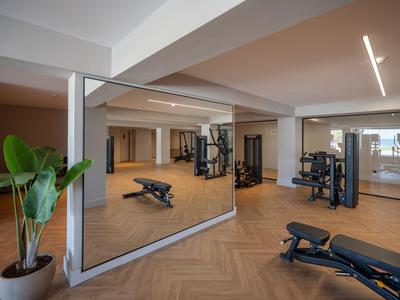 Moderner Fitnessbereich mit Hantelbänken, Geräten und großen Spiegeln in Hotelumgebung.