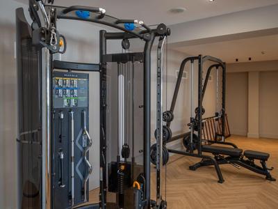 Moderner Fitnessraum mit multifunktionalem Trainingsgerät und Sitzbank auf Parkettboden.