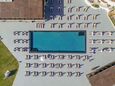 Drohnenaufnahme eines rechteckigen Pools mit Sonnenliegen auf gepflastertem Bereich neben grüner Wiese.