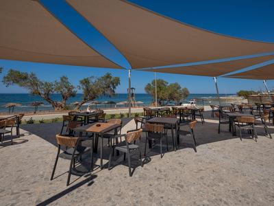 Terrassenbereich eines Hotels am Meer mit Tischen, Stühlen und schattenspendenden Segeln.